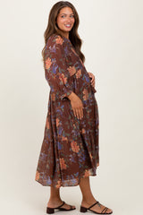 woman wearing a brown floral maternity dress with long sleeves and a flowing skirt, holding her baby bump
