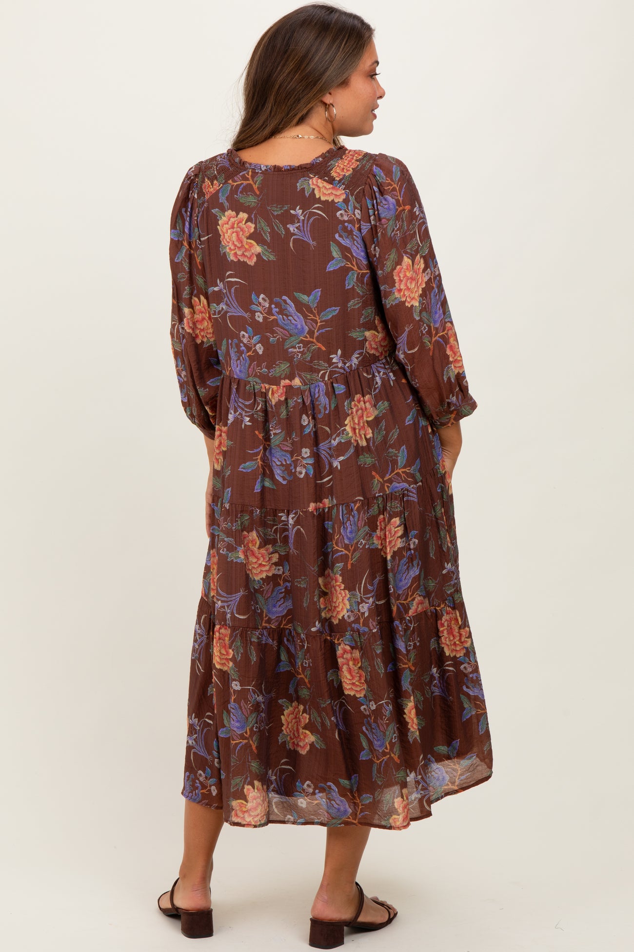 woman wearing a brown floral maternity dress with long sleeves and a tiered skirt, showing a baby bump