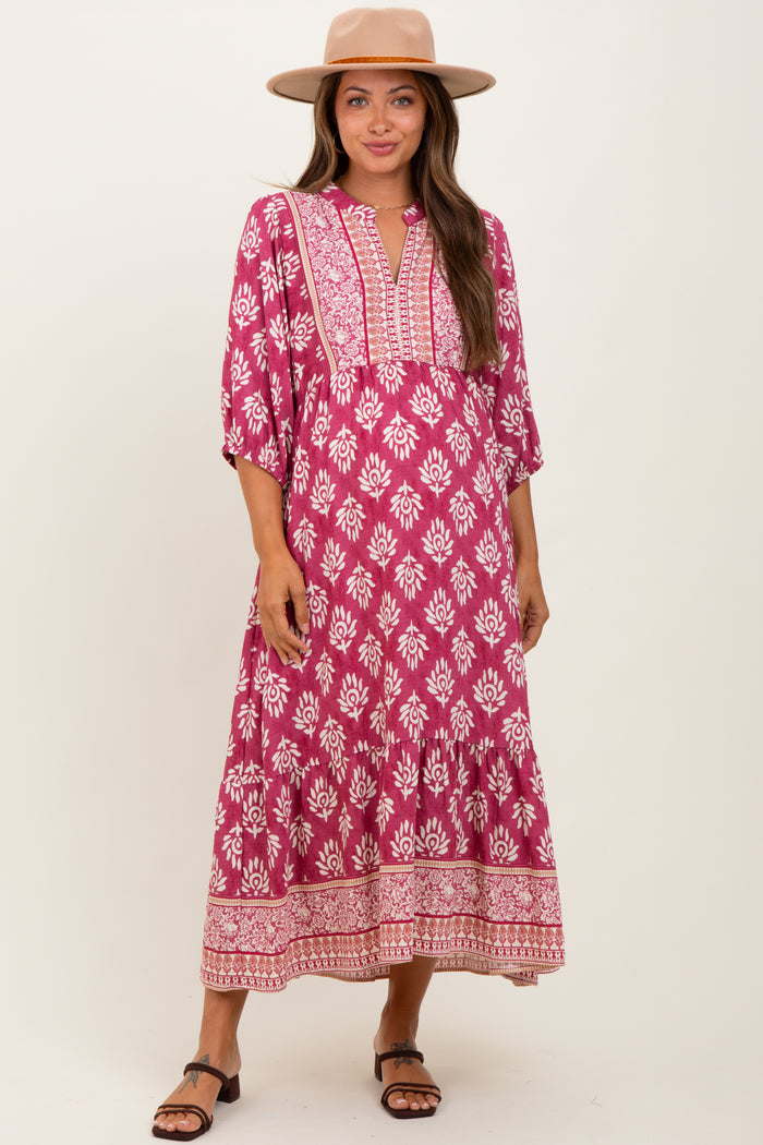 woman wearing a pink and white floral print maternity maxi dress with bell sleeves and a v-neckline, smiling and posing with a hat