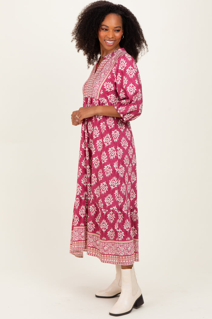 woman wearing a pink floral maxi dress with three-quarter sleeves and embroidery details, standing and smiling