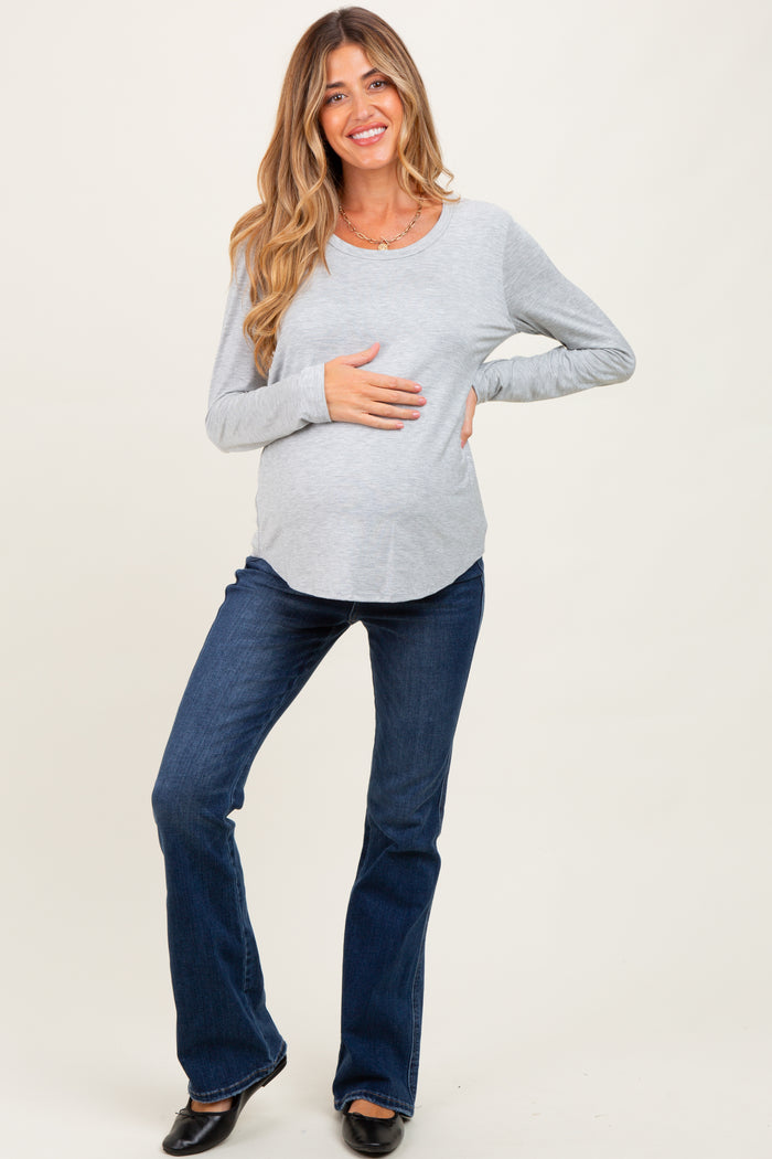 woman wearing a gray long sleeve maternity top and flared jeans, holding her baby bump