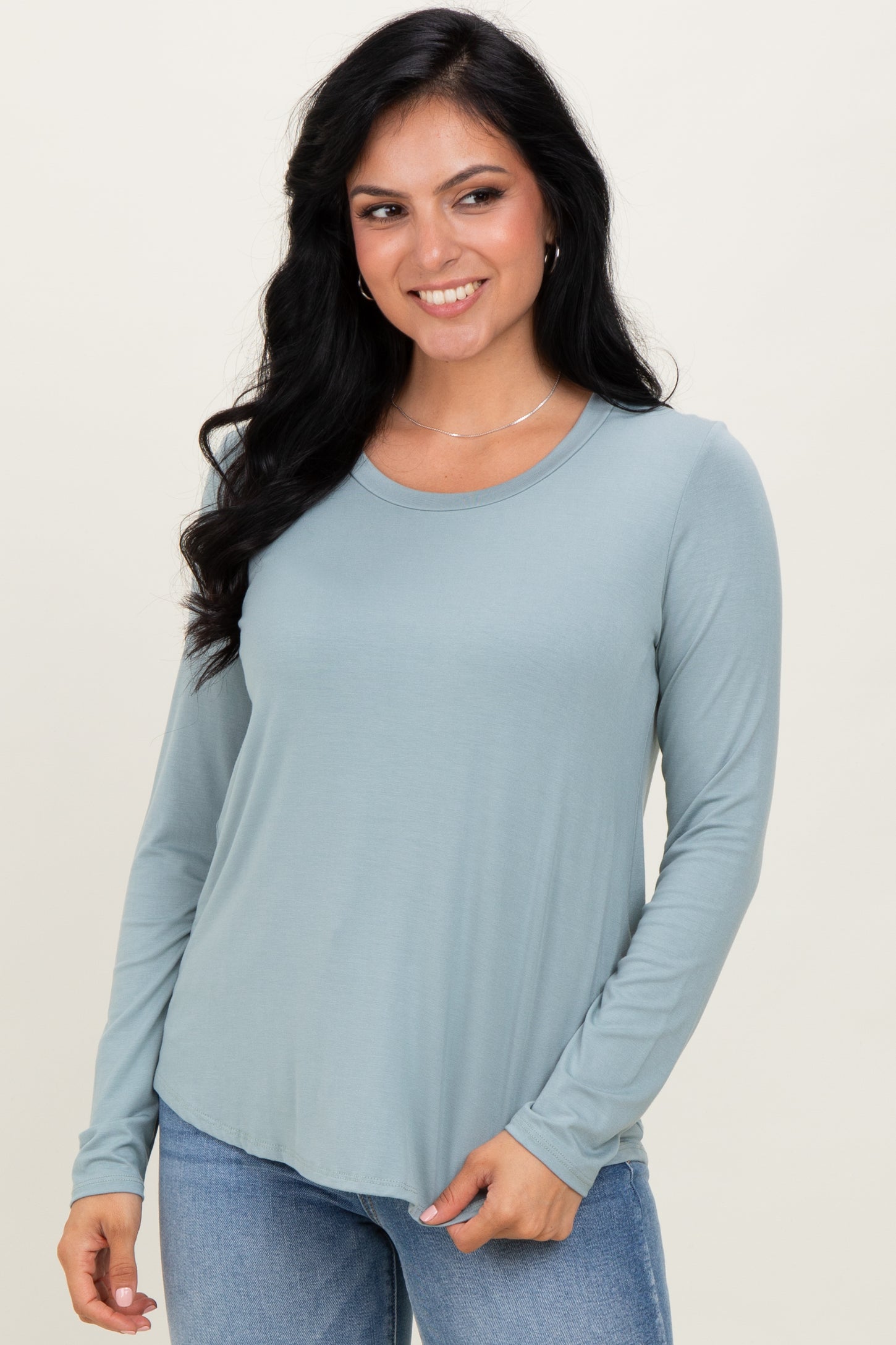 woman wearing a light blue long sleeve top with a rounded neckline and casual fit, standing and smiling