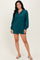 woman wearing a teal zip-up sweatshirt dress with long sleeves and a relaxed fit, standing in a light pose