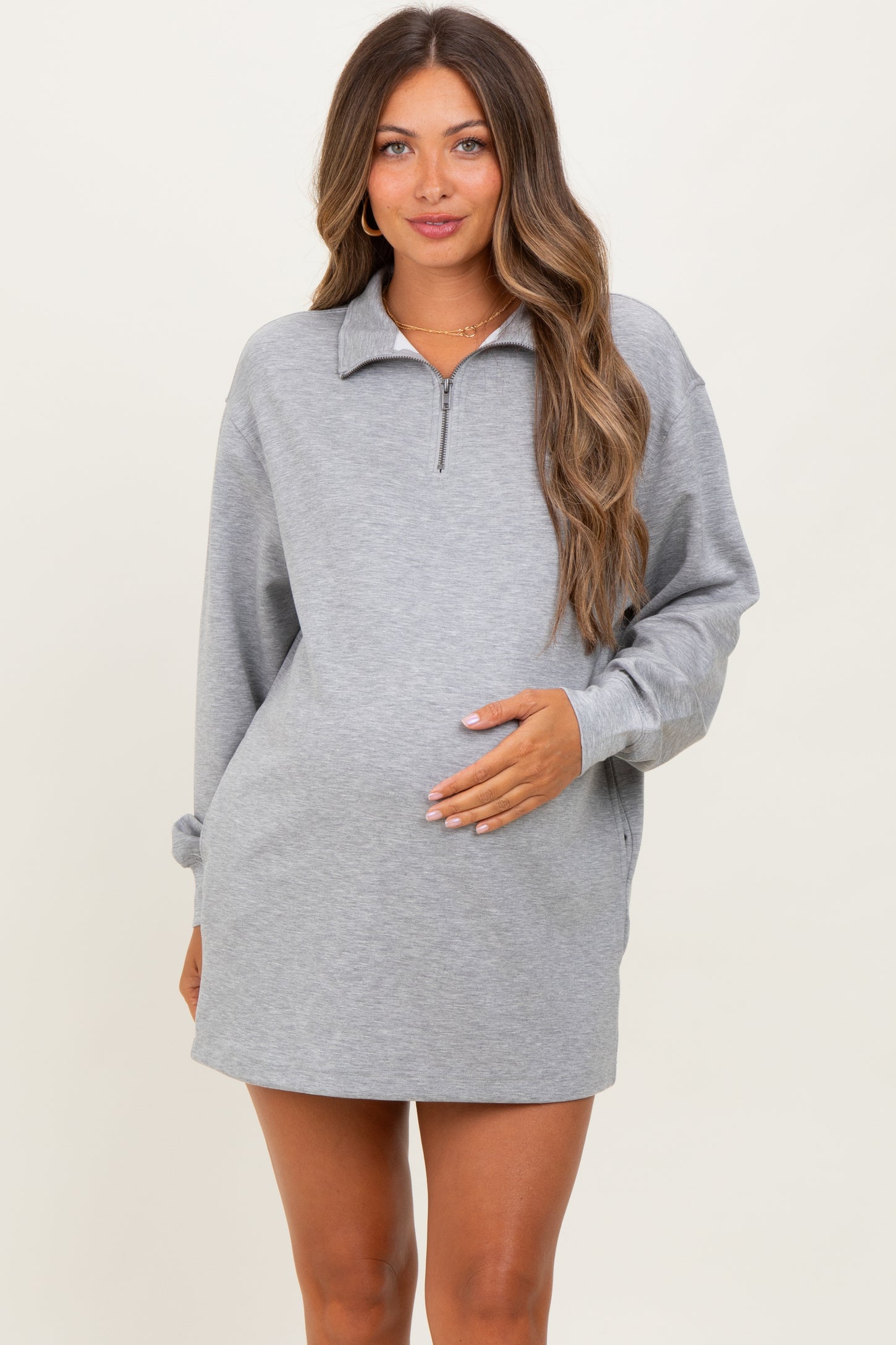 woman wearing a gray maternity quarter-zip sweatshirt dress and holding her baby bump