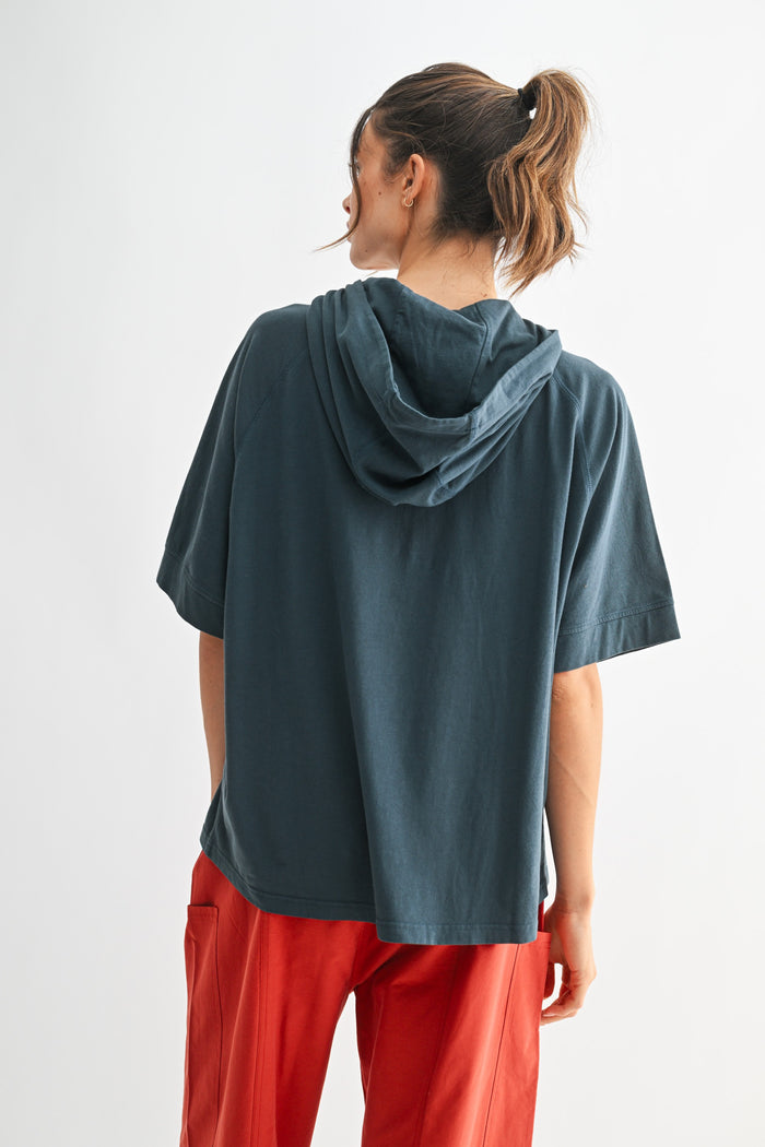 woman wearing a dark teal oversized hoodie with a hood, styled with loose red trousers from the back