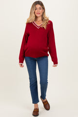 woman wearing a red v-neck maternity sweater with white stripes and blue jeans, showing her baby bump