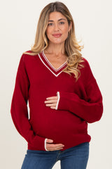 woman wearing a red v-neck maternity sweater with white trim and holding her baby bump