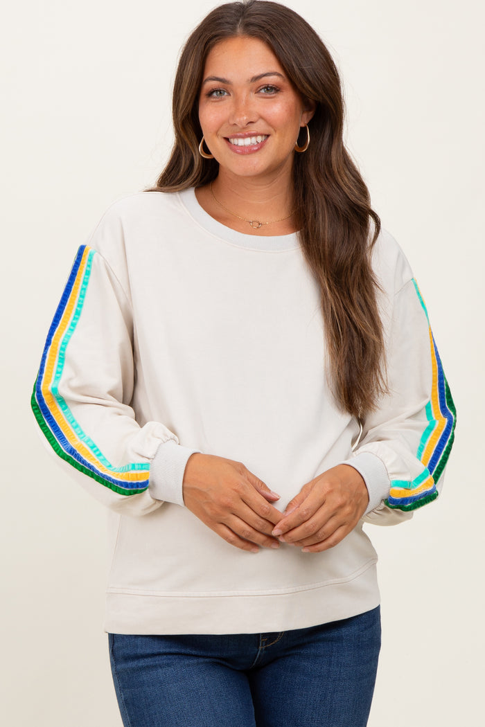 woman wearing a cream maternity sweatshirt with colorful striped sleeves and a relaxed fit, smiling at the camera