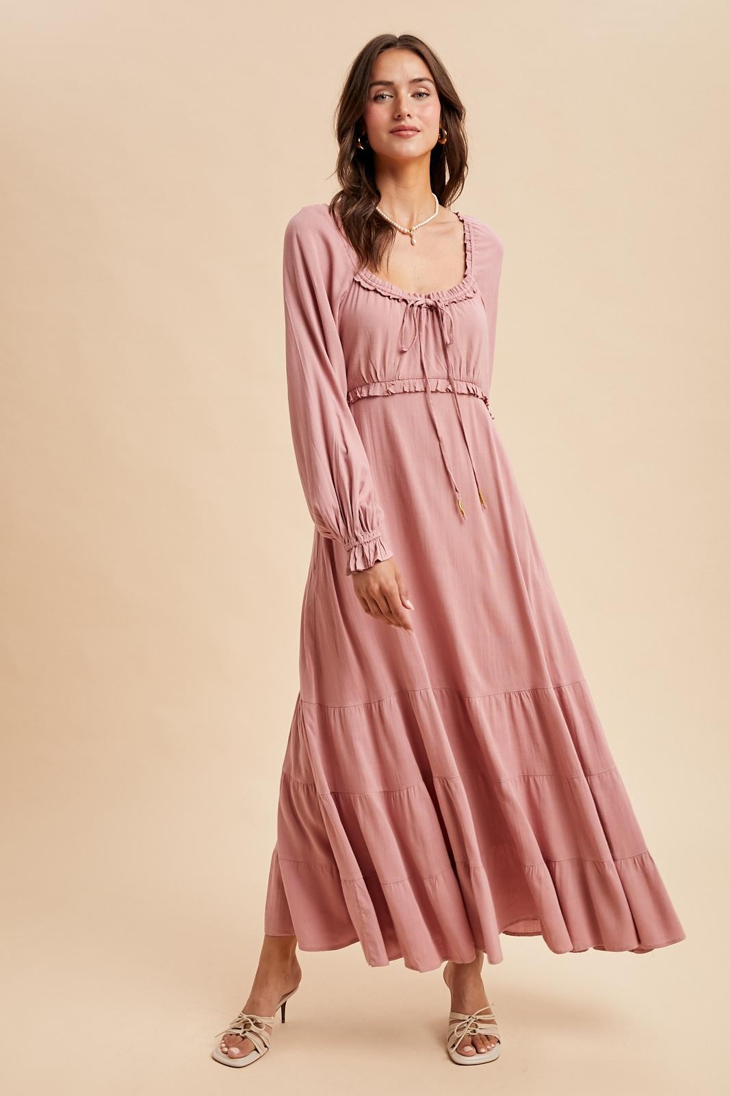 woman wearing a blush pink long sleeve maxi dress with a tie front and tiered skirt