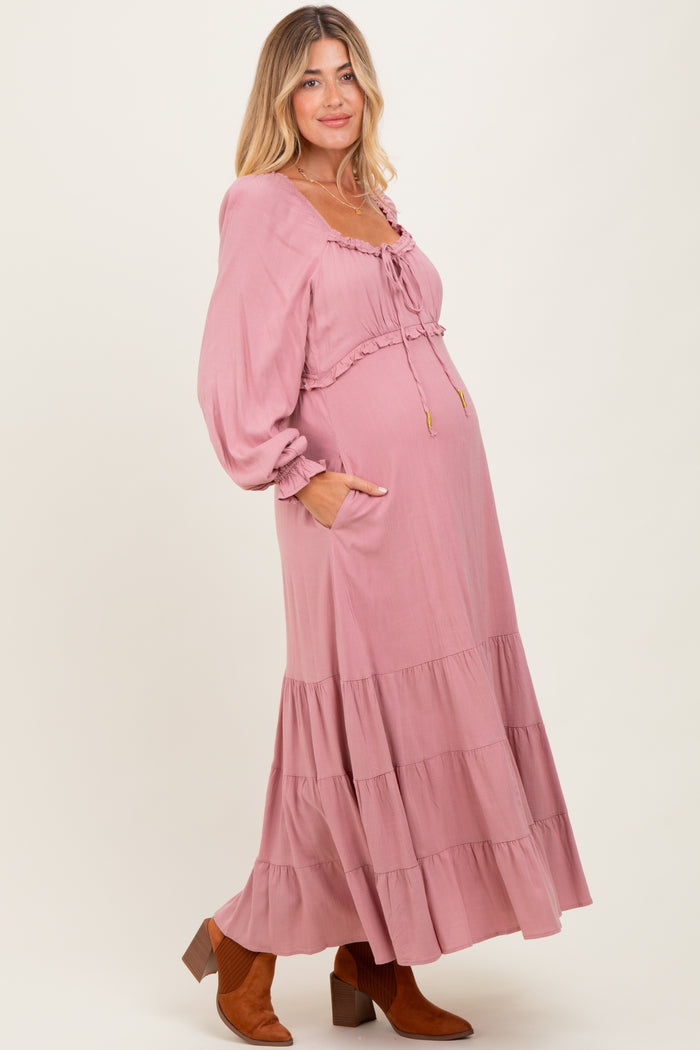 woman wearing a pink maternity maxi dress with puff sleeves and tiered skirt, showing her baby bump and standing in profile