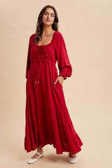 woman wearing a red maxi dress with a cinched waist, long sleeves, and ruffle details