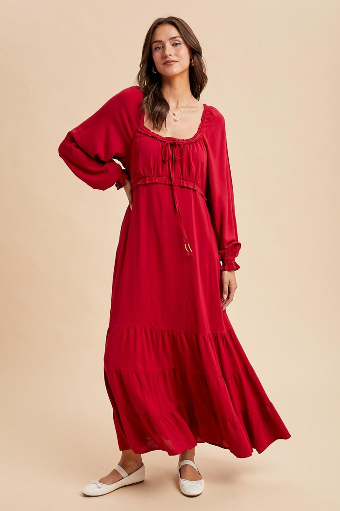 woman wearing a red long sleeve maxi dress with a cinched bodice and tiered skirt, styled with white flats