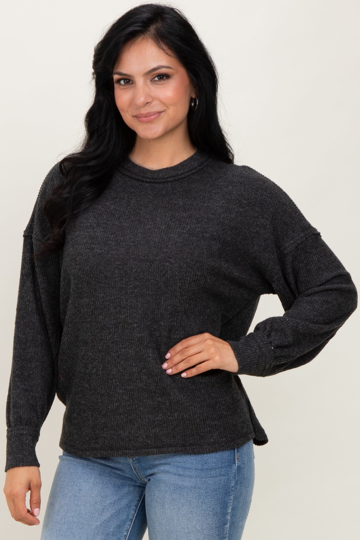 woman wearing a dark gray oversized sweater with long sleeves and side slits, paired with light blue jeans