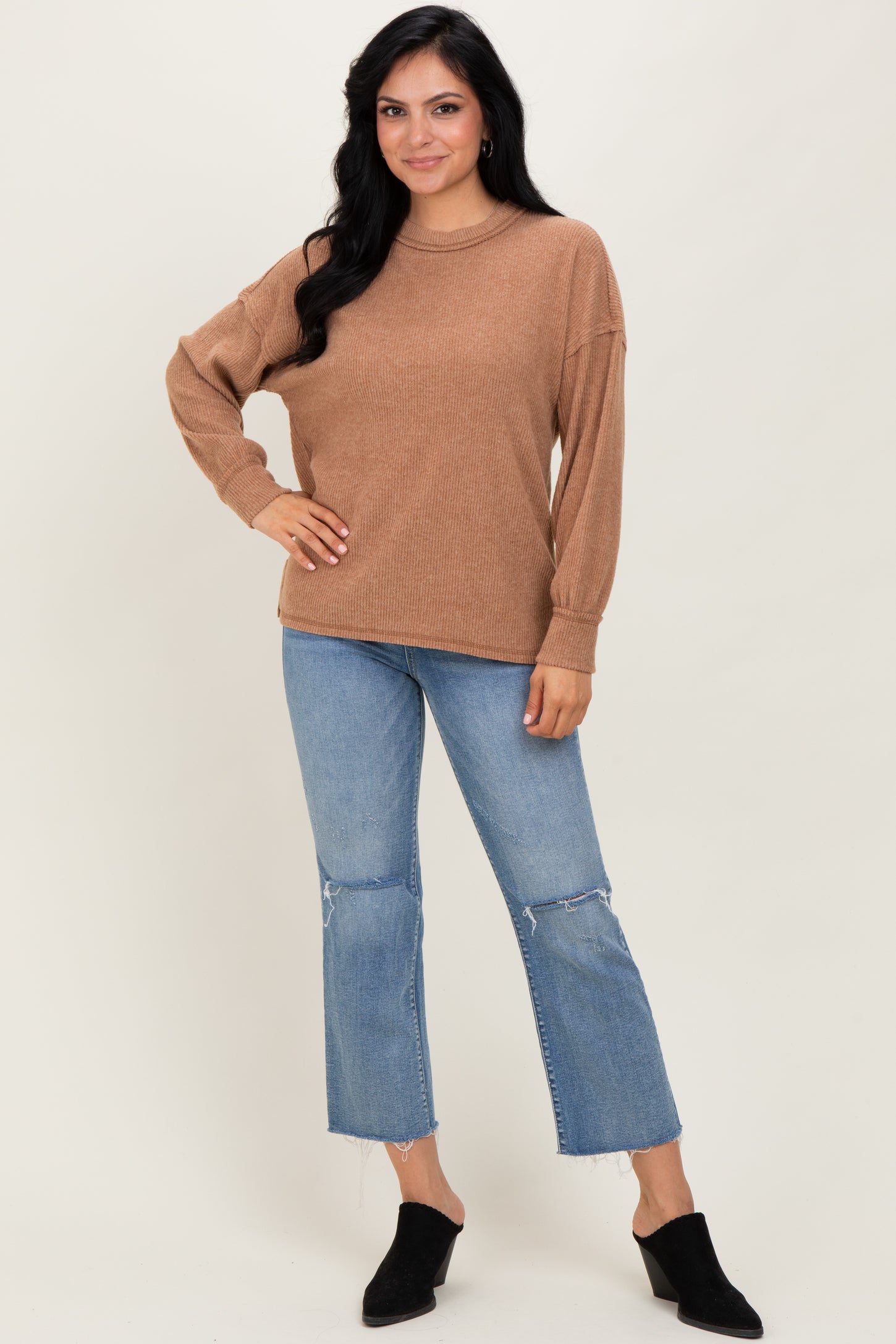 woman wearing a brown oversized sweater with long sleeves and blue distressed denim cropped jeans