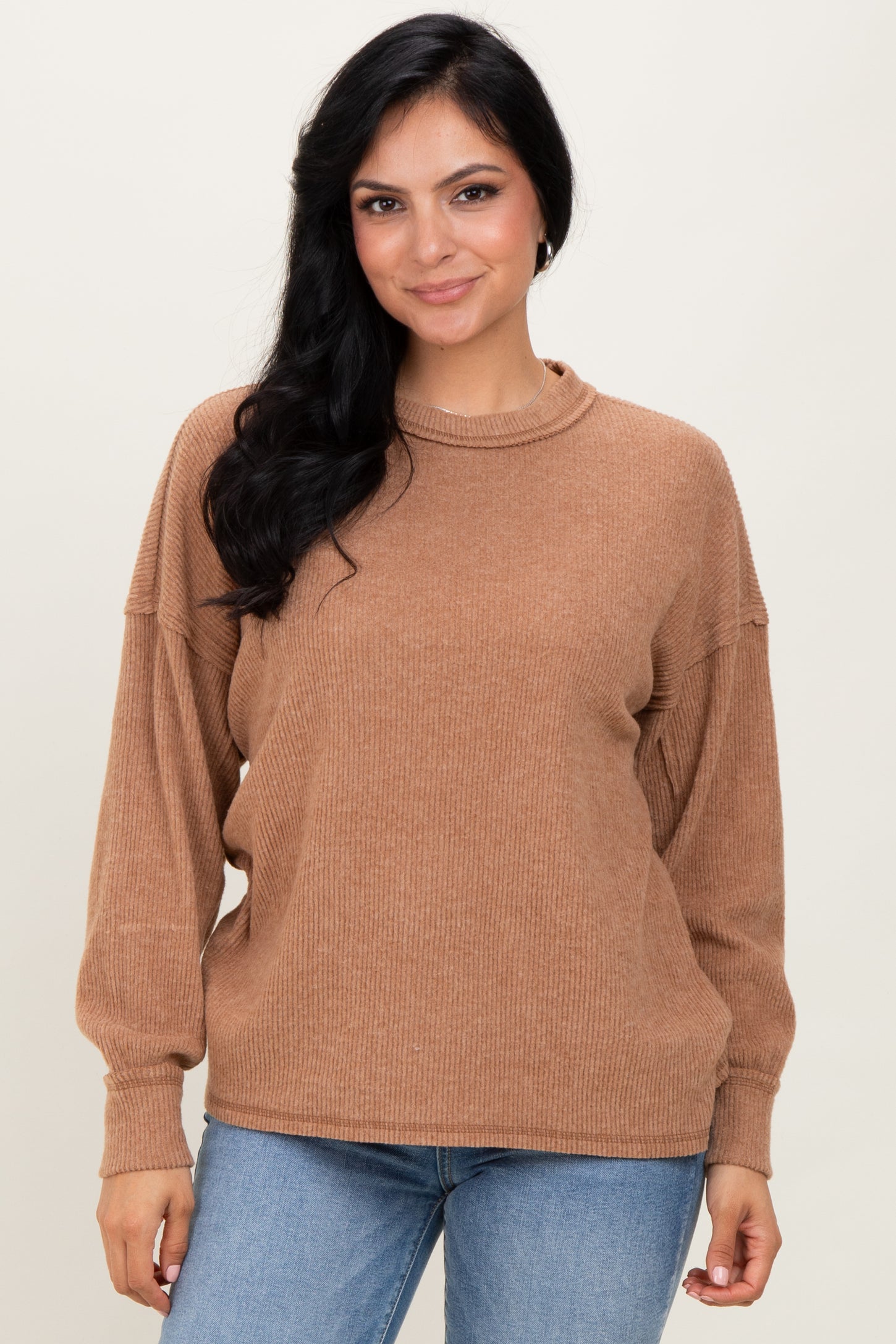 woman wearing a tan ribbed long sleeve sweater with a high neckline and relaxed fit, paired with blue jeans