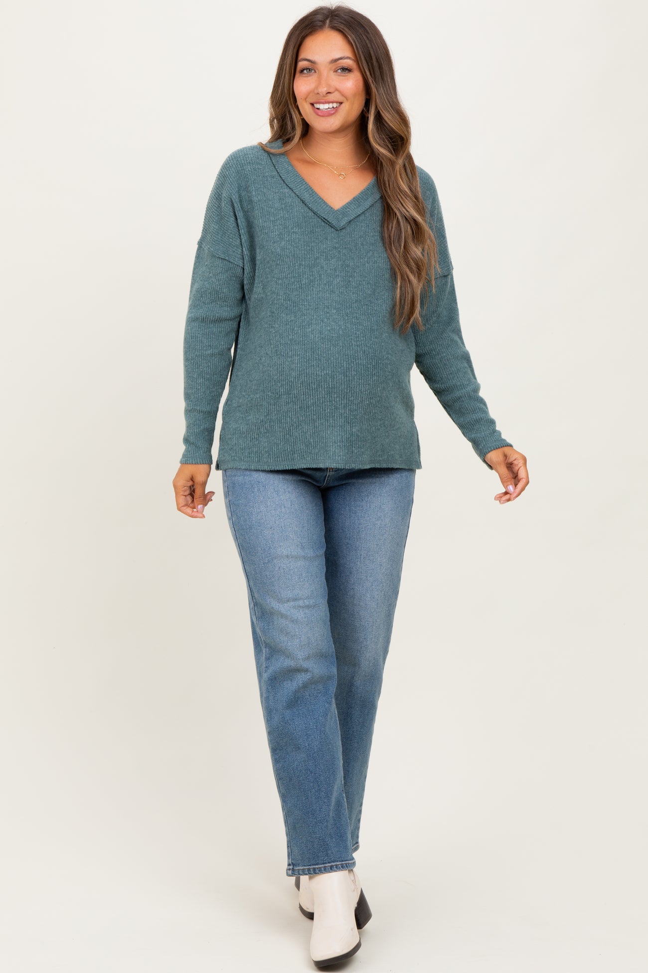 woman wearing a teal v-neck maternity sweater and blue jeans, with a visible baby bump