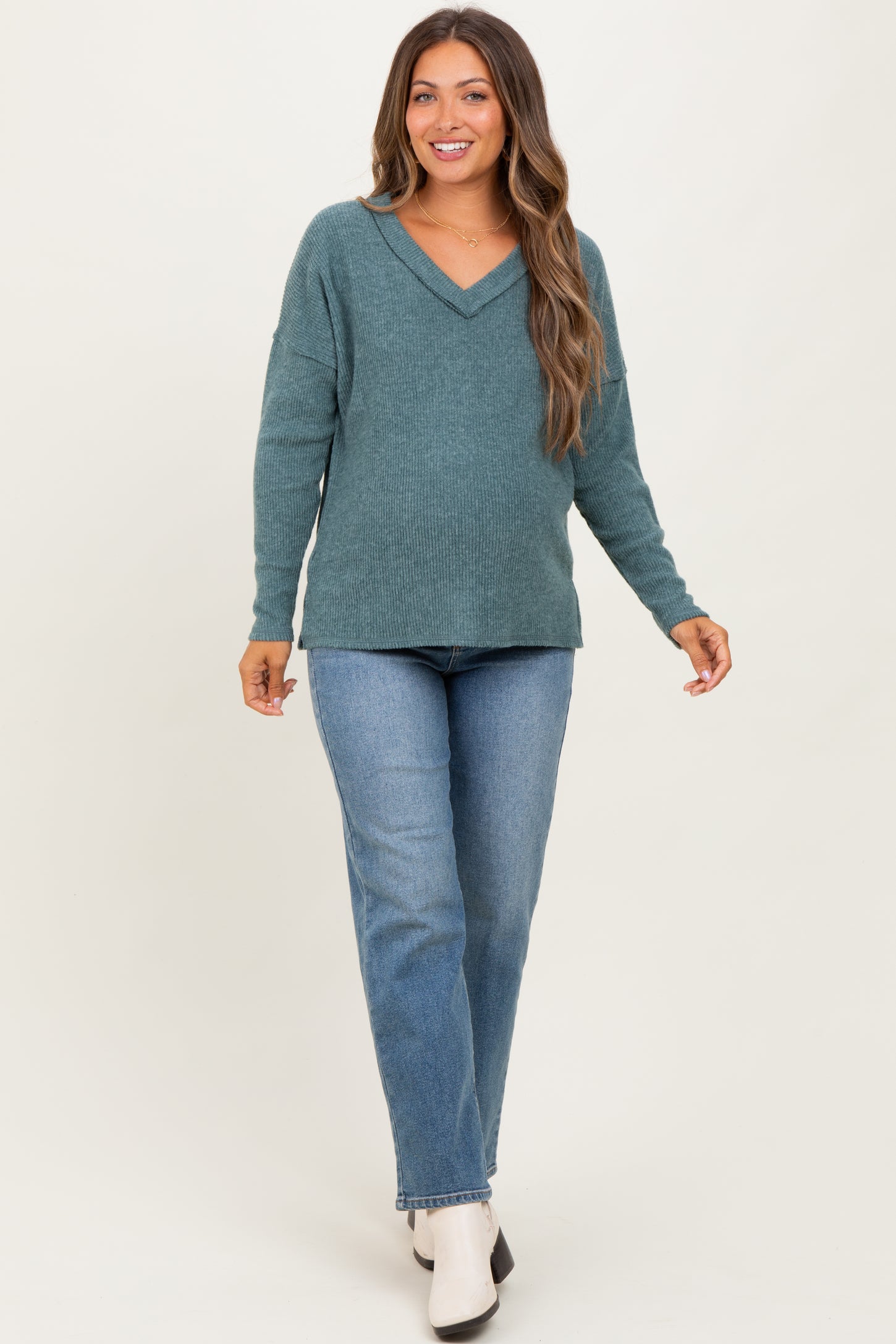 woman wearing a teal v-neck maternity sweater and blue jeans, with a visible baby bump