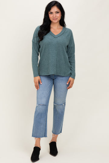 woman wearing a teal v-neck sweater with relaxed fit and distressed straight leg jeans, paired with black ankle boots
