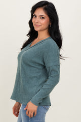 woman wearing a teal long sleeve v-neck sweater with a relaxed fit and side slits, standing against a neutral background