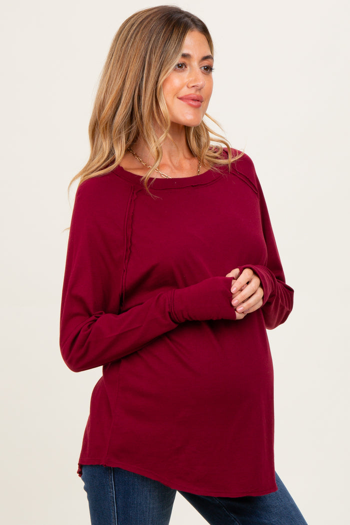woman wearing a burgundy long sleeve maternity top with side ruching and holding her baby bump