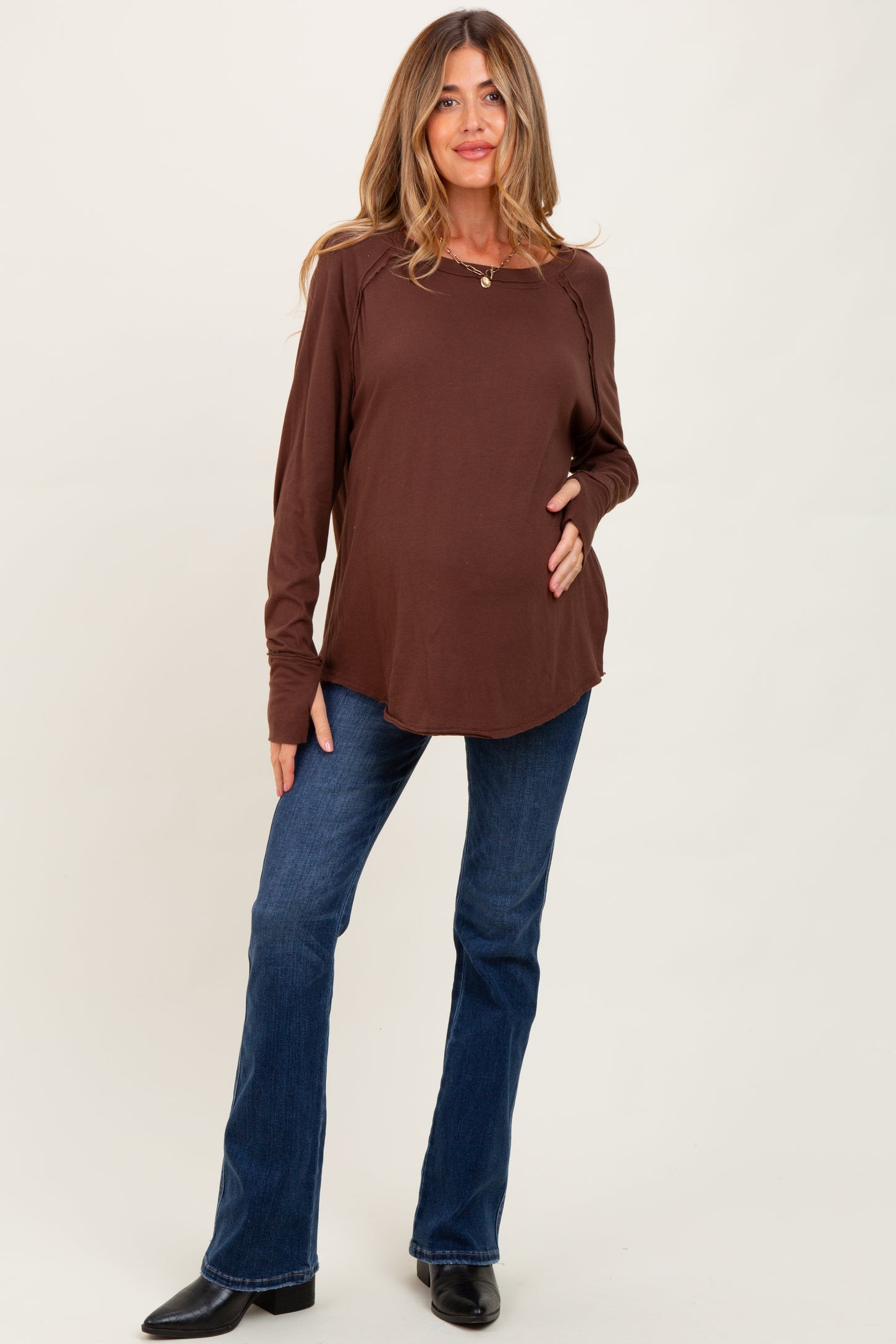 woman wearing a brown long sleeve maternity top and holding her baby bump with blue flared jeans