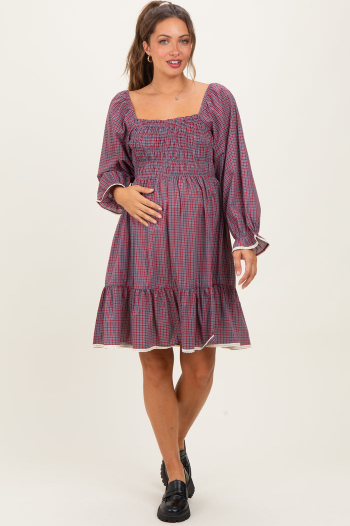 woman wearing a red and navy checkered maternity dress with a smocked bodice and tiered skirt, showing her baby bump