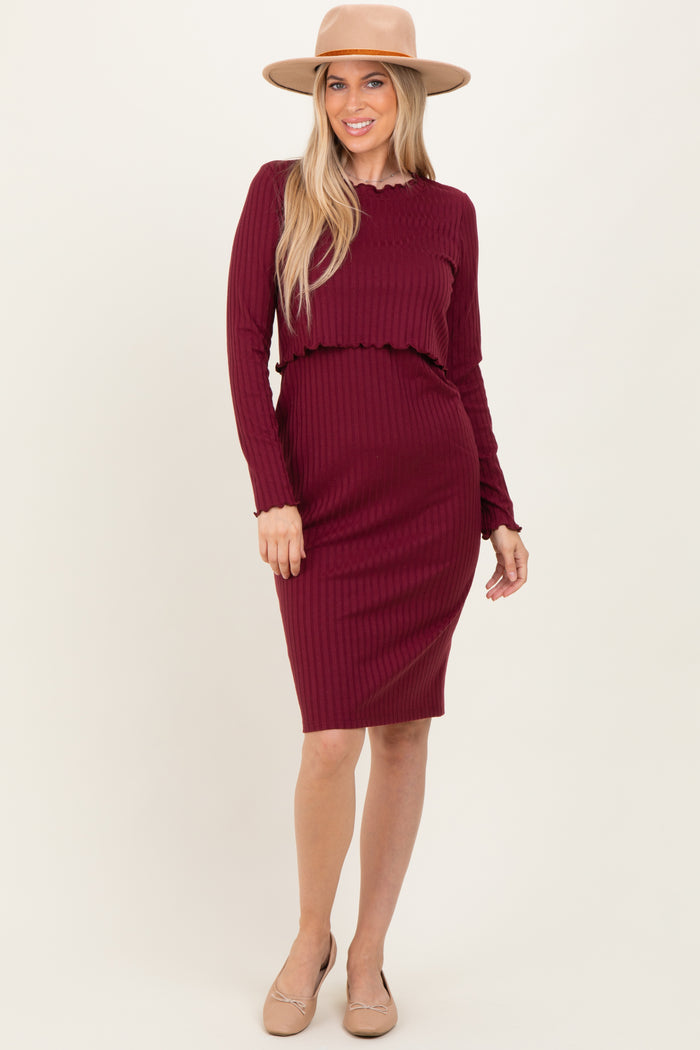 woman wearing a burgundy ribbed long sleeve dress with a ruffled waist and a wide-brimmed hat