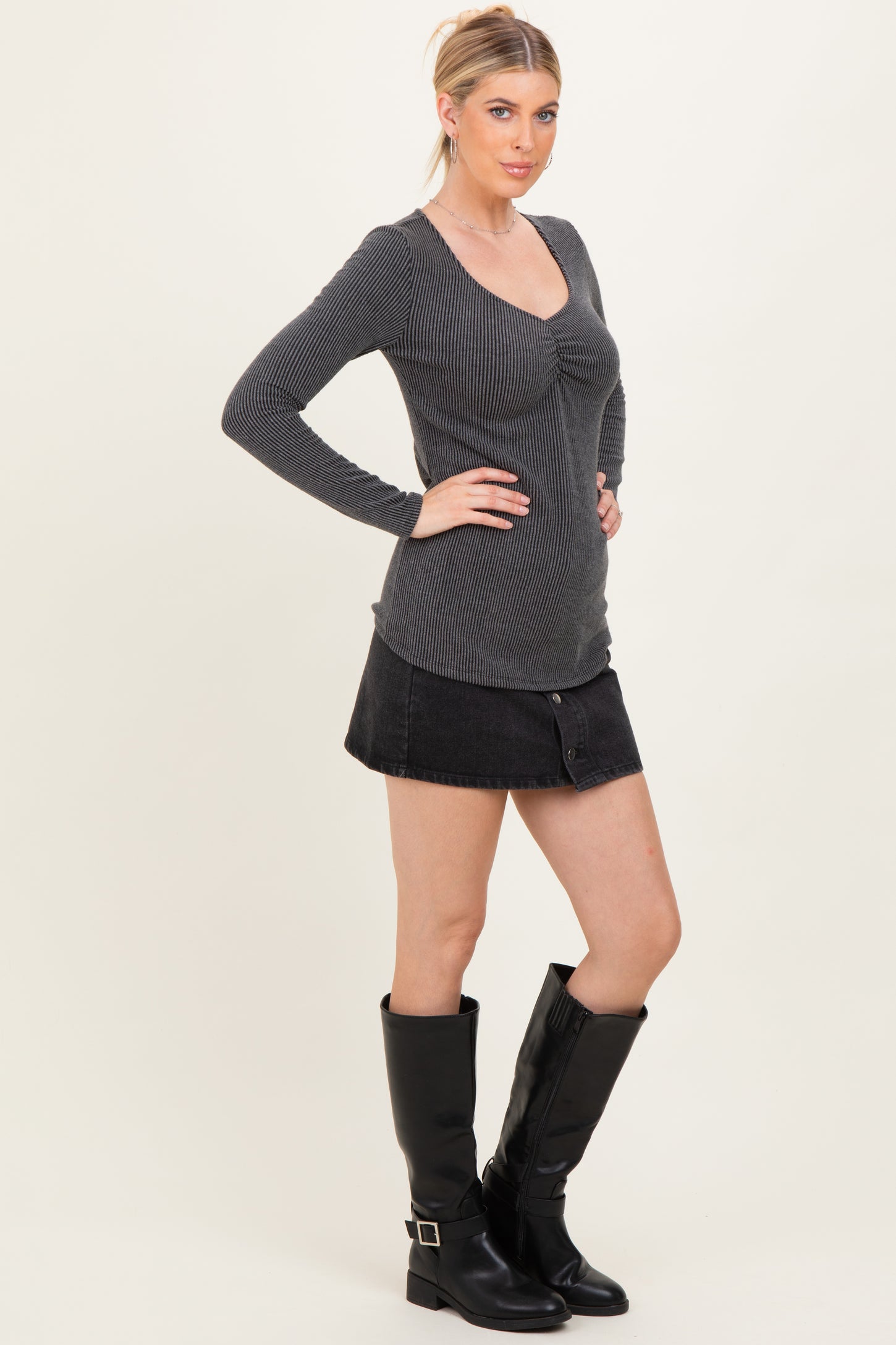 woman wearing a gray ribbed long sleeve top with a scoop neckline and a black denim mini skirt, paired with black knee-high boots