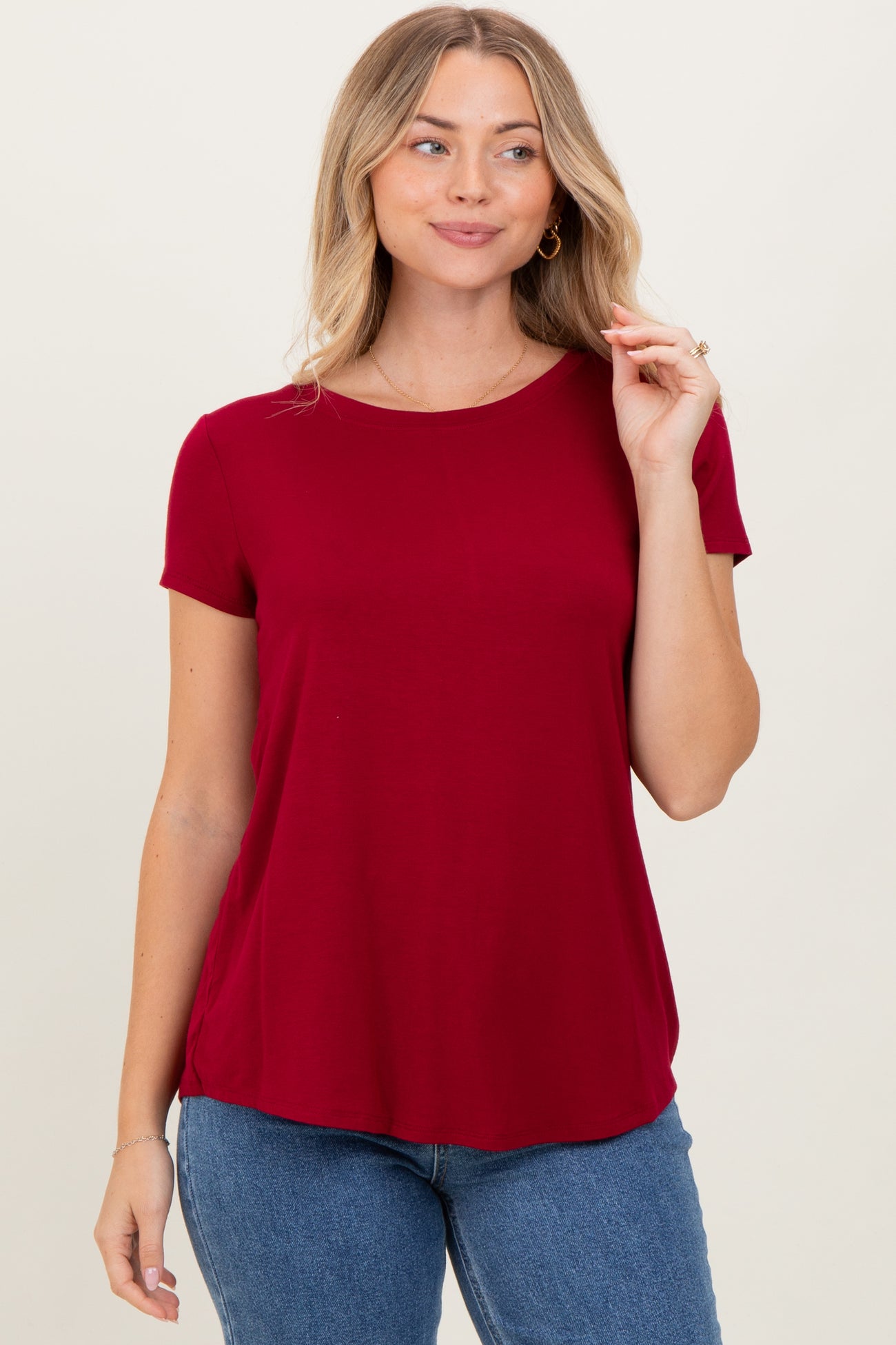 woman wearing a burgundy short sleeve top with a relaxed fit and round neckline paired with blue jeans