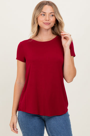 woman wearing a burgundy short sleeve top with a relaxed fit and round neckline paired with blue jeans