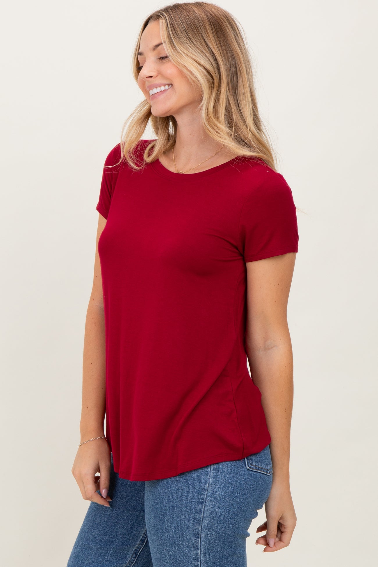 woman wearing a fitted burgundy short sleeve top paired with jeans, smiling against a light background