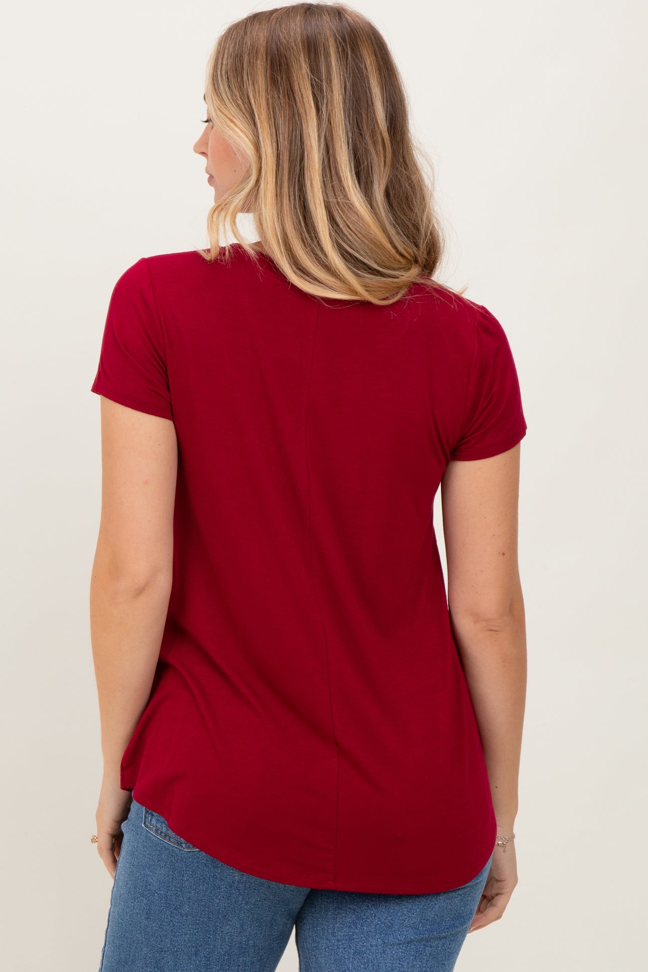 woman wearing a red short sleeve top with a curved hem and back seam detail, facing away from the camera