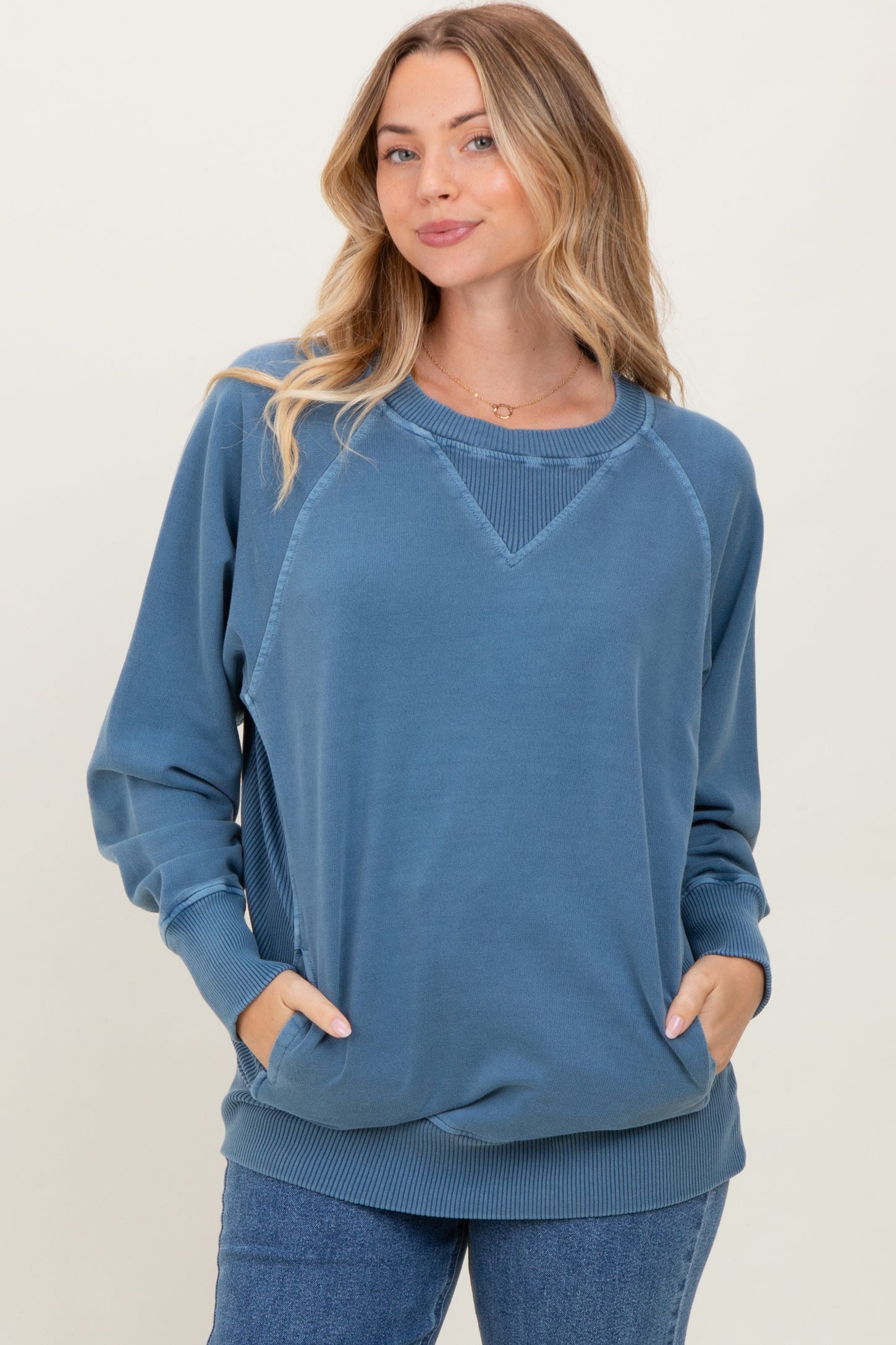 woman wearing a blue long sleeve sweatshirt with a relaxed fit and pockets, posing confidently