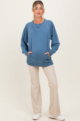 woman wearing a blue maternity sweatshirt with a relaxed fit and front pockets, paired with light beige pants and a baby bump visible