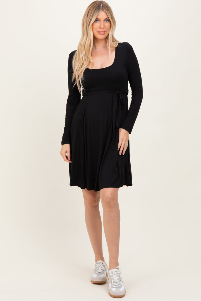 woman wearing a black long sleeve wrap dress with a tie detail at the waist and white sneakers