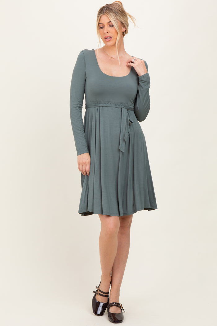 woman wearing a long sleeve sage green dress with a scoop neckline and a tie belt at the waist