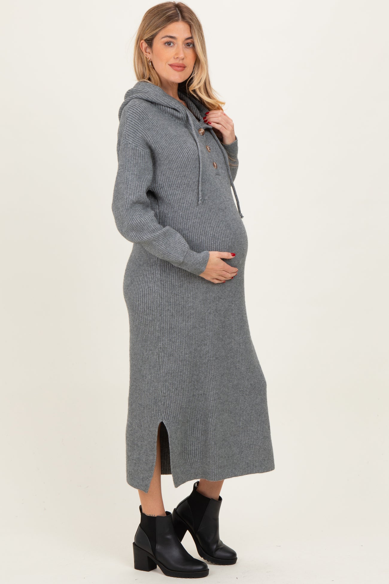 woman wearing a grey knit maternity hoodie dress with a side split and holding her baby bump