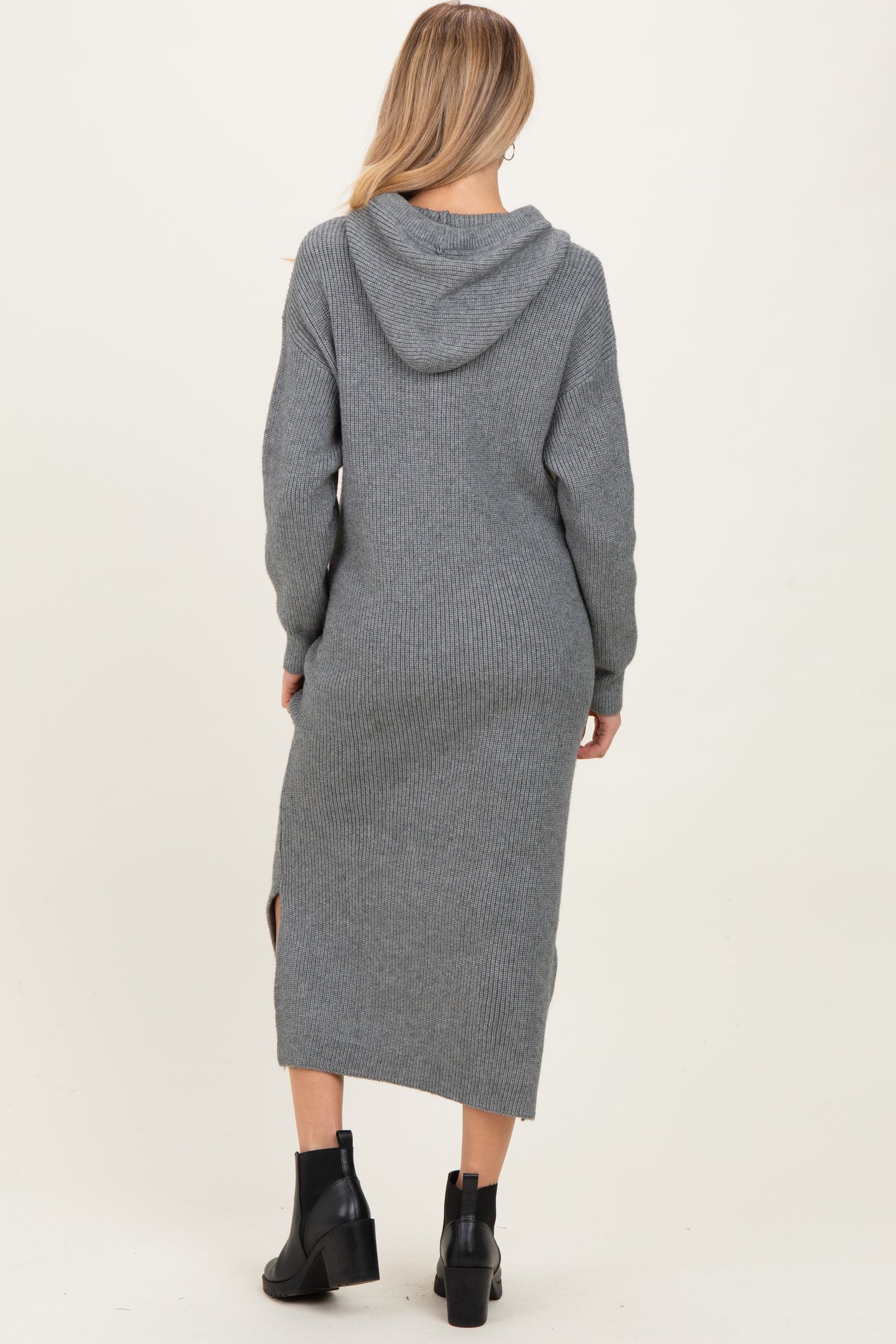 woman wearing a gray knitted maternity sweater dress with a hood and side slits, showing her baby bump from the back