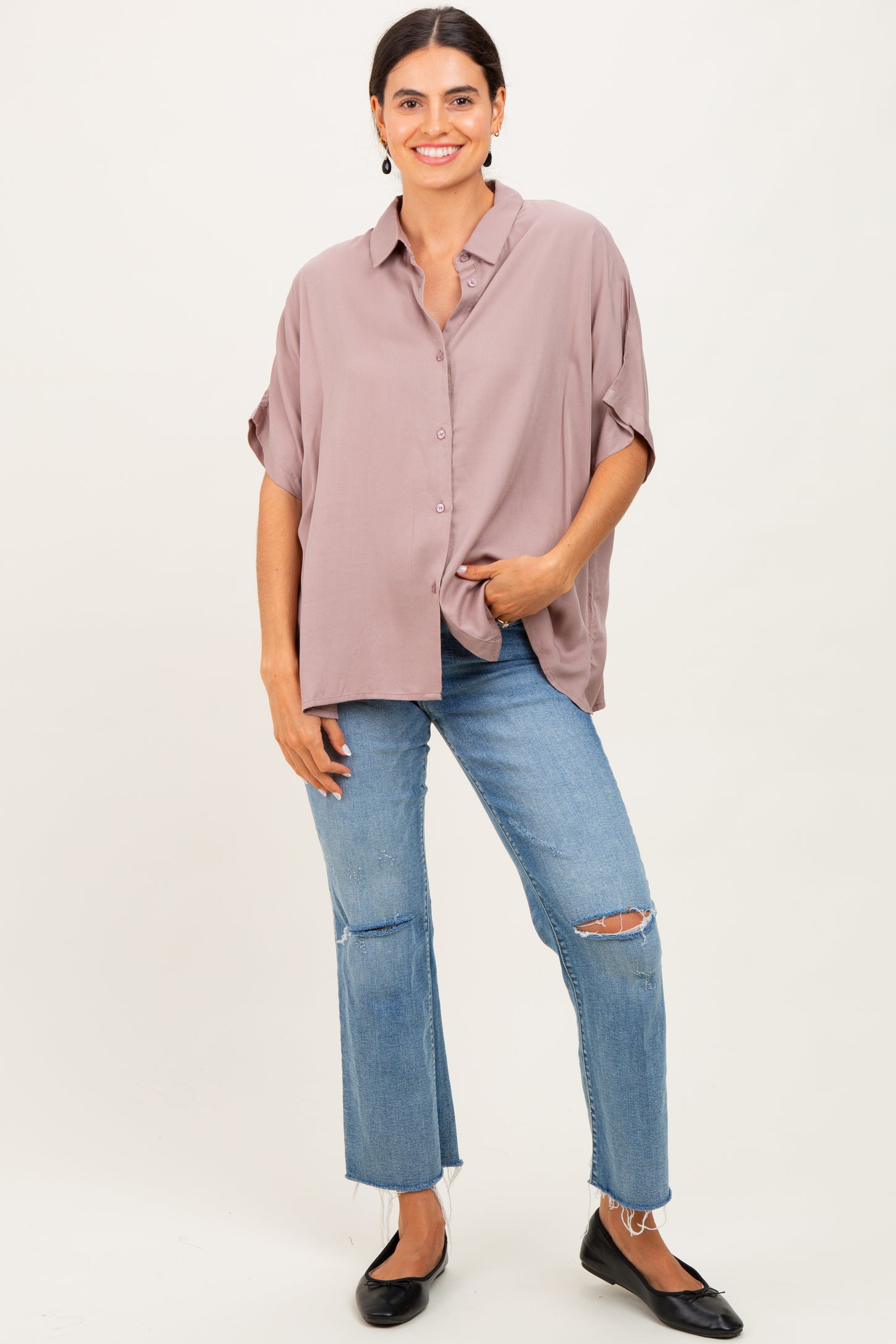 woman wearing a mauve oversized button-up shirt and distressed light wash jeans with black flats