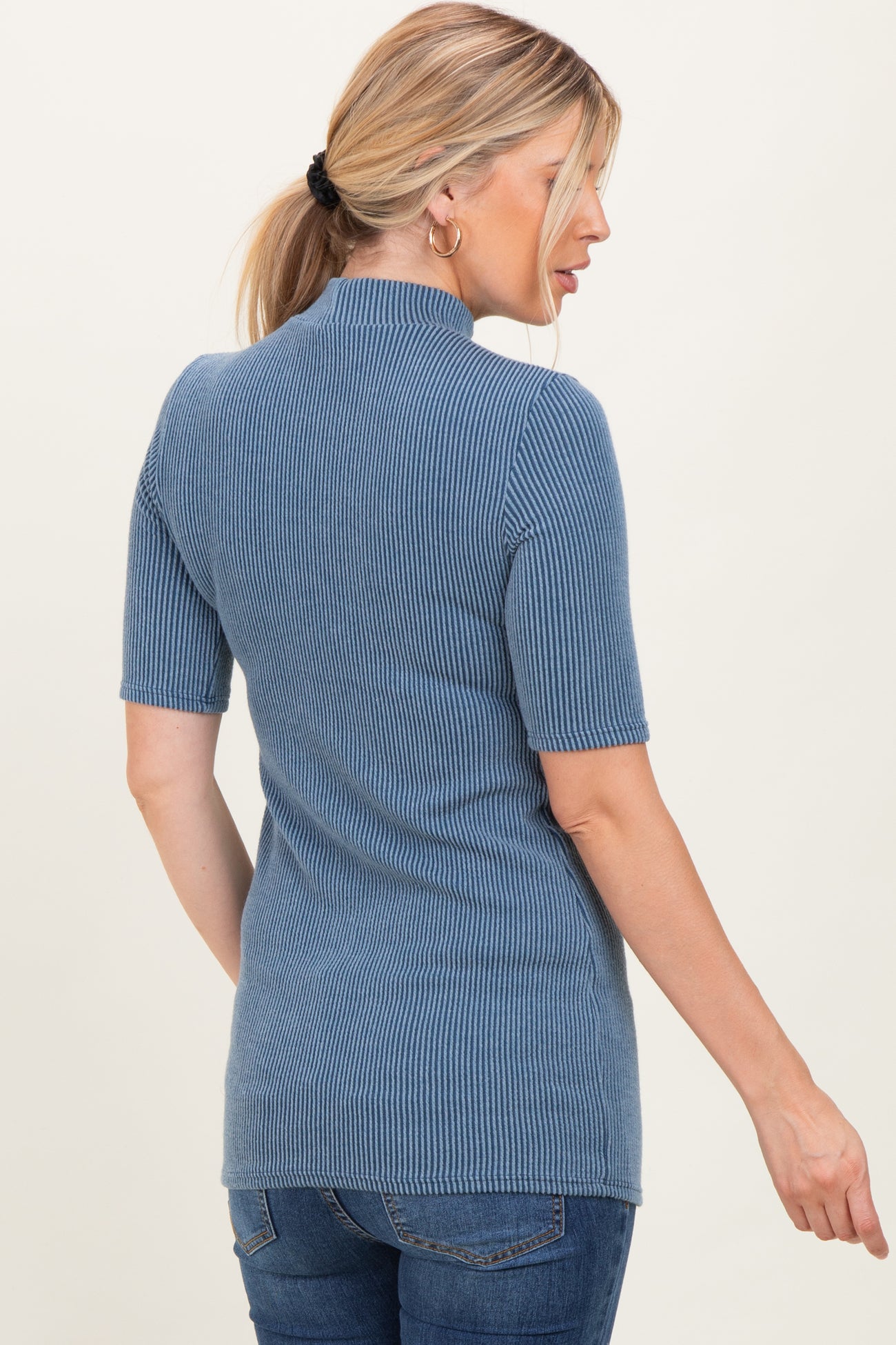 woman wearing a ribbed blue short sleeve top with a high neck and fitted silhouette
