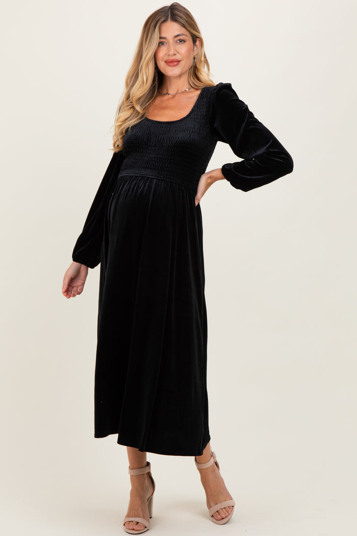 woman wearing a black smocked maternity dress with long sleeves and a fitted bodice, showcasing a baby bump