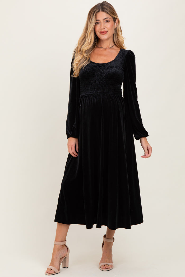 woman wearing a black velvet maternity dress with long sleeves and a fitted bodice, showing a baby bump