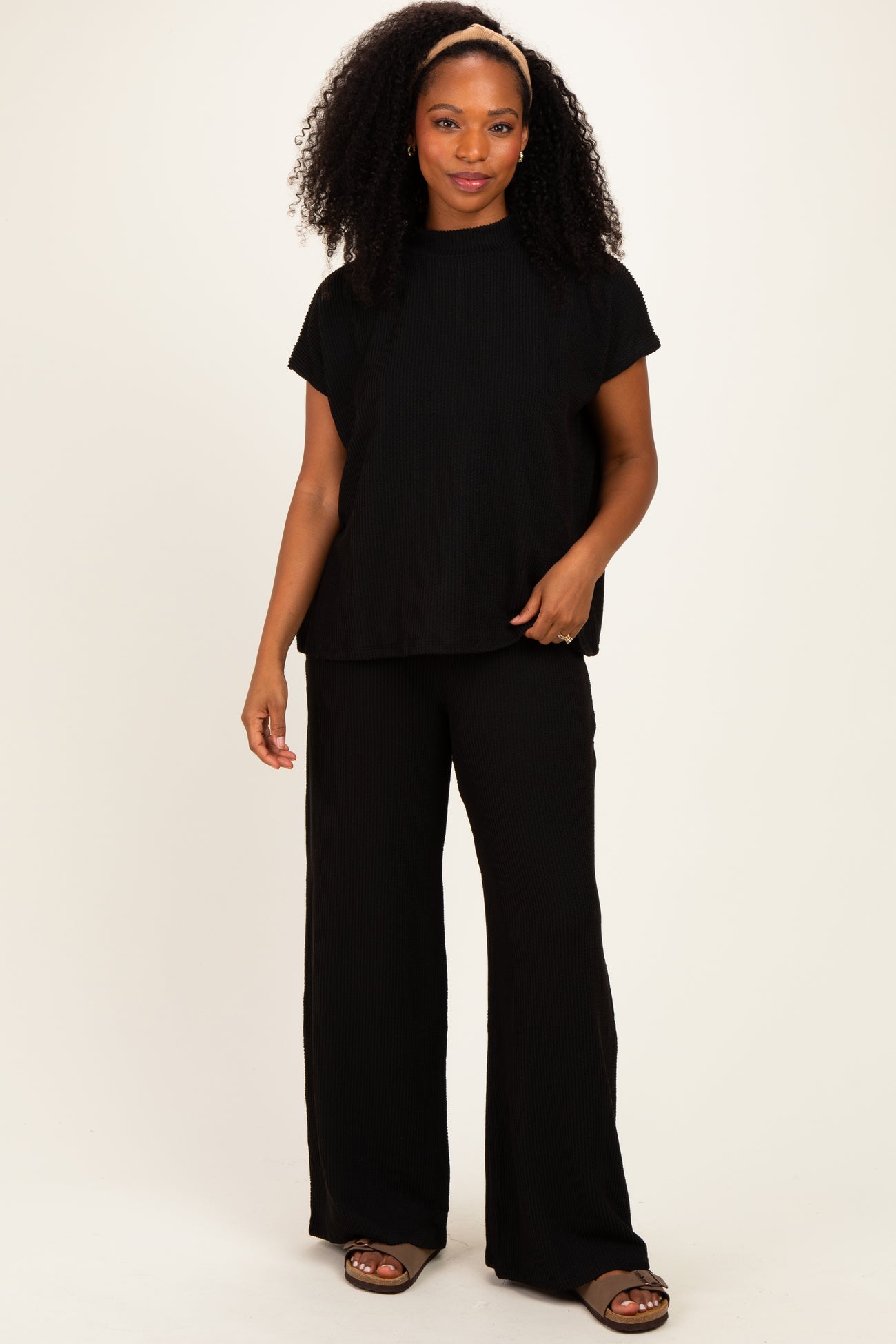 woman wearing a black ribbed short sleeve top and matching wide-leg pants, standing with one hand on her hip