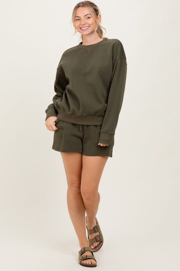 woman wearing an olive green oversized sweatshirt and matching shorts, paired with brown sandals