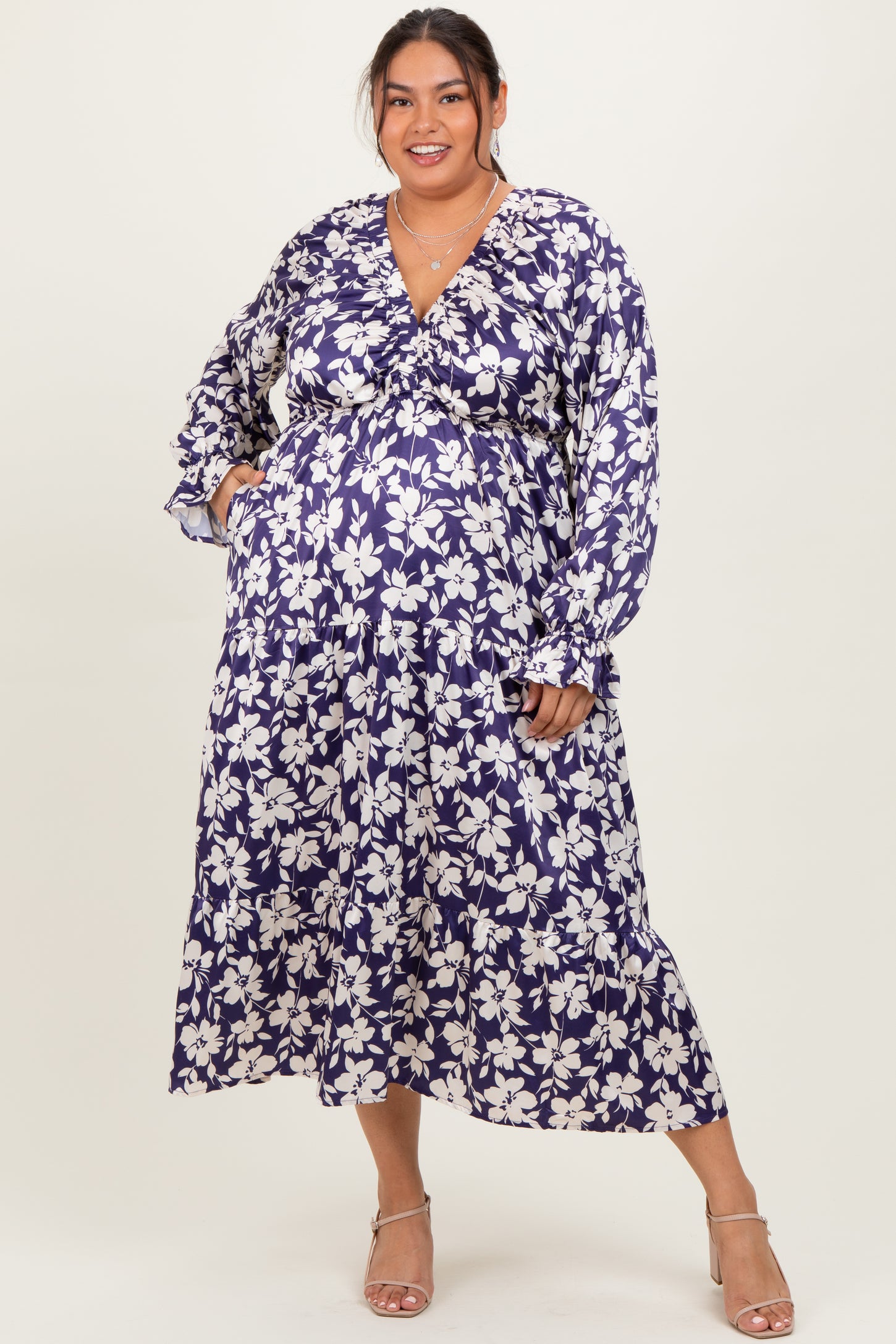 woman wearing a purple floral plus size maternity maxi dress with long sleeves and pockets, showing her baby bump