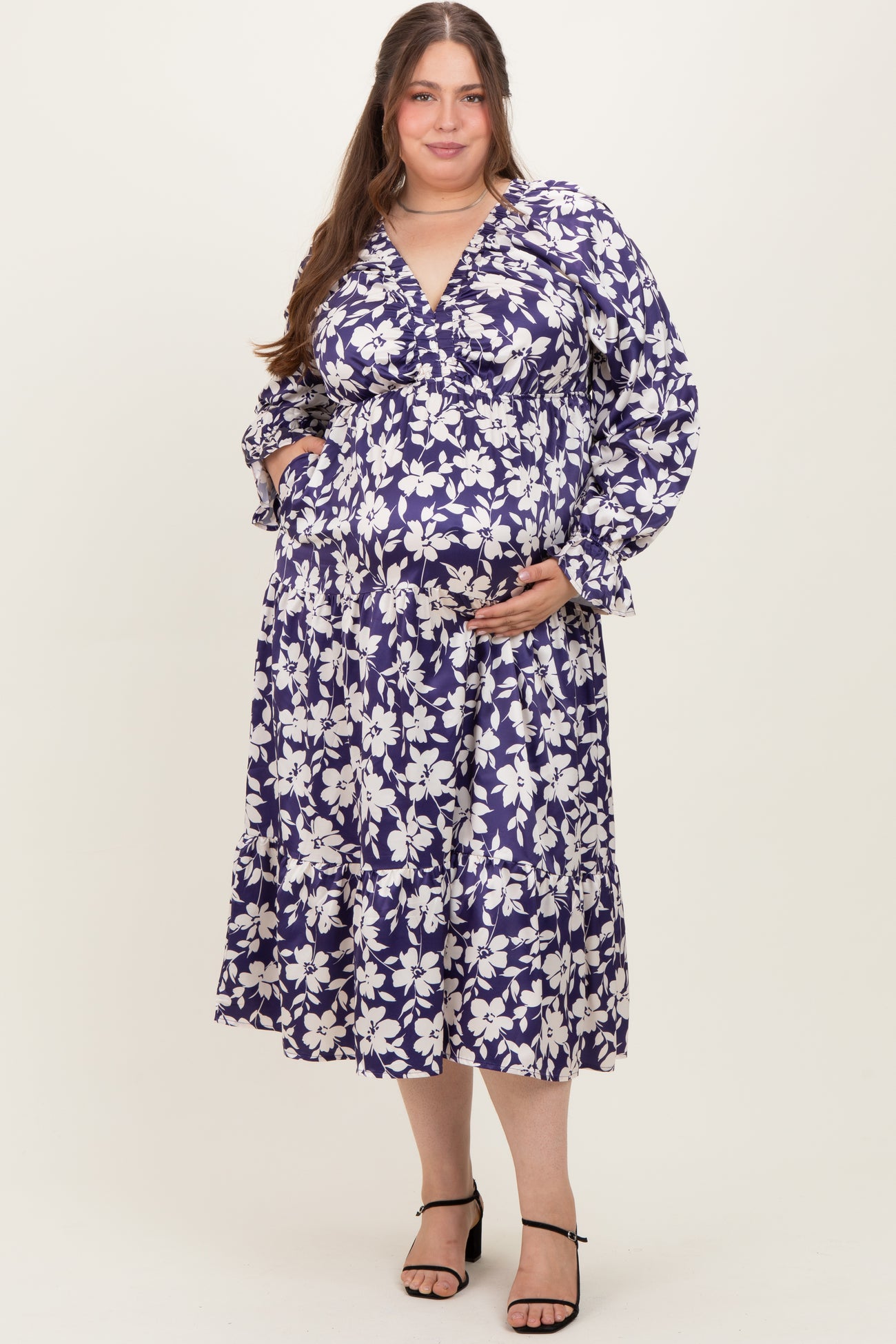 woman wearing a purple floral maternity dress with long sleeves and a tiered skirt, showing her baby bump