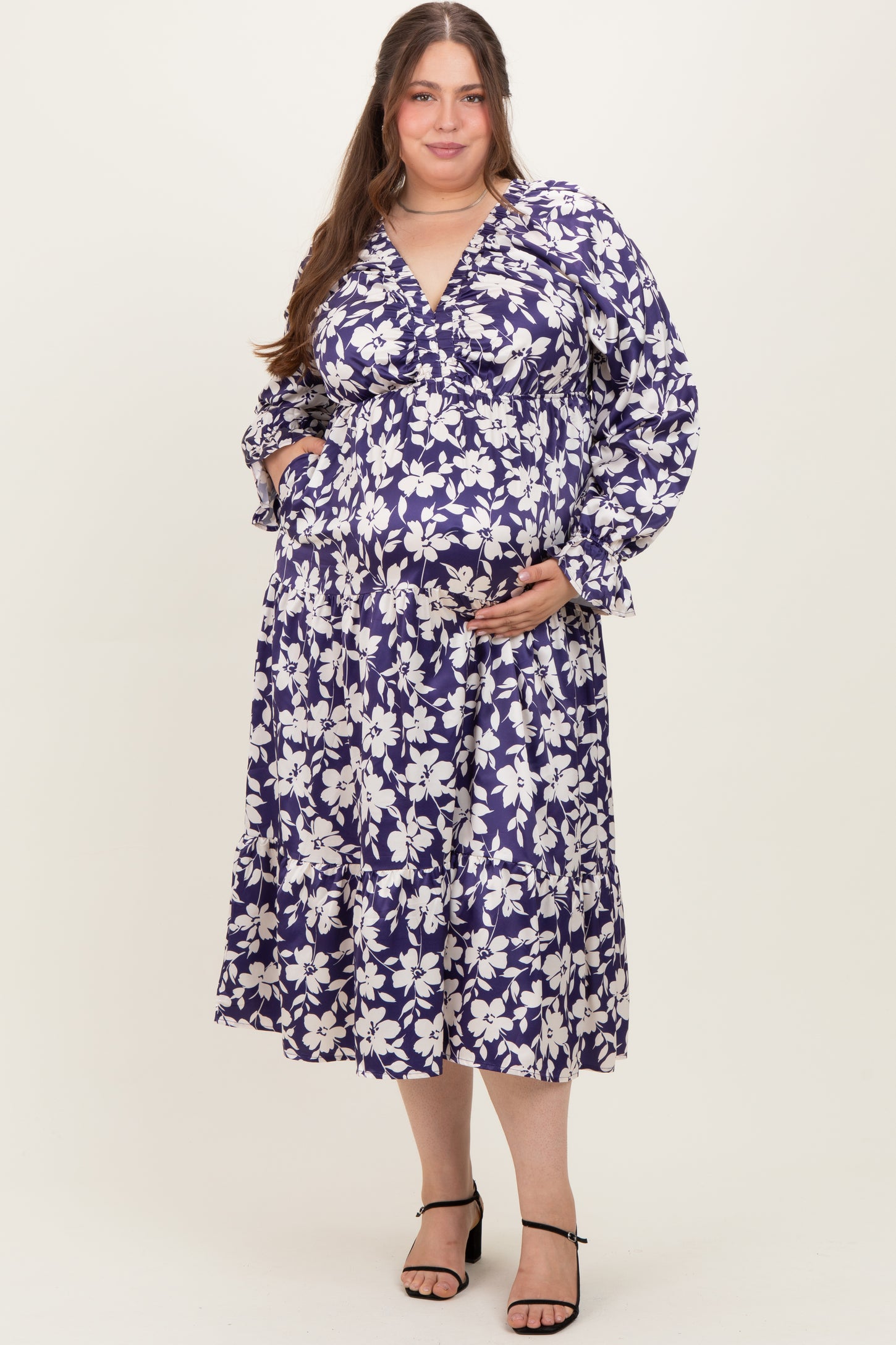 woman wearing a purple floral maternity dress with long sleeves and a tiered skirt, showing her baby bump