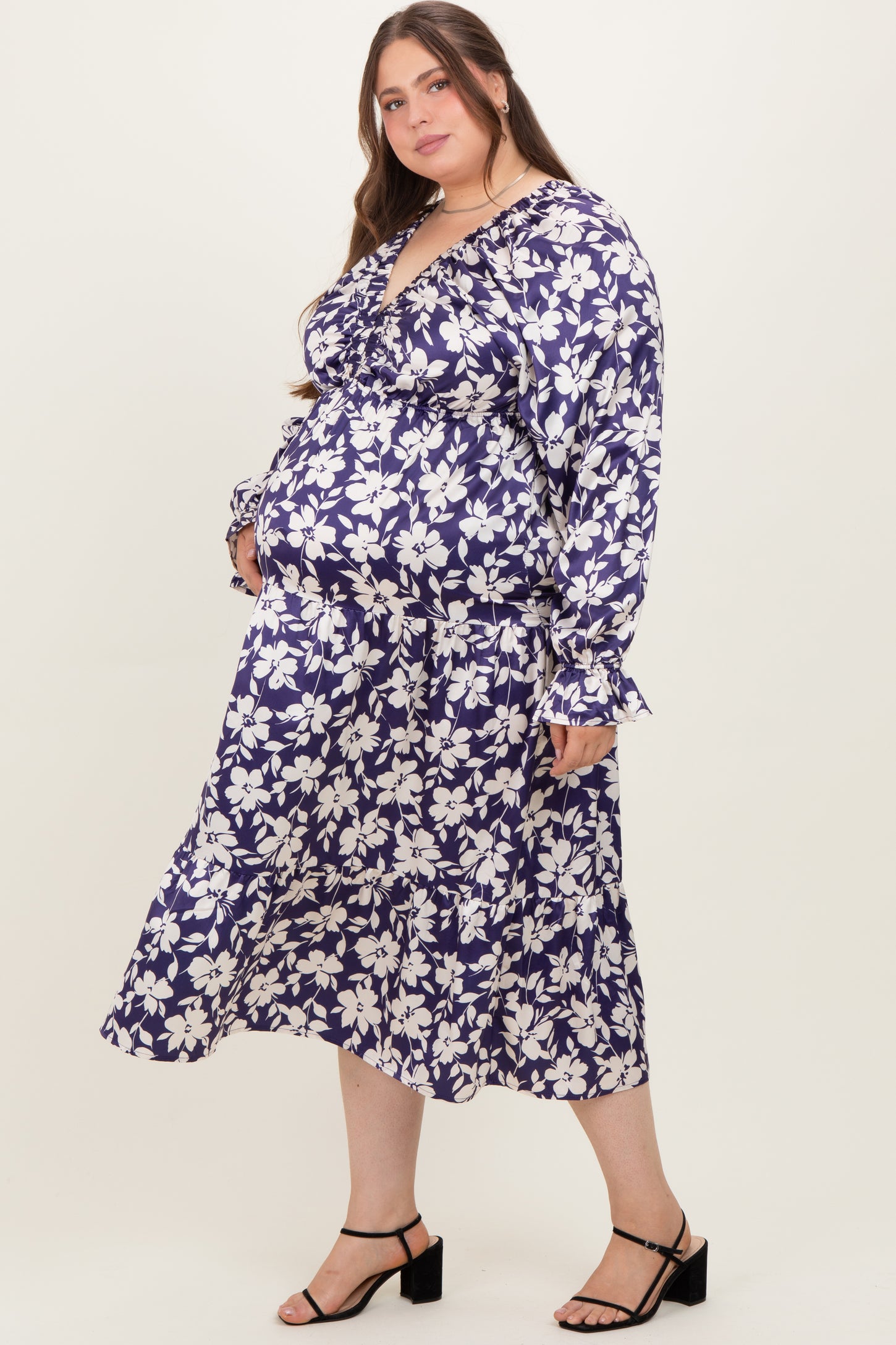 woman wearing a navy blue floral maternity dress with long sleeves and a ruffled hem, showing her baby bump