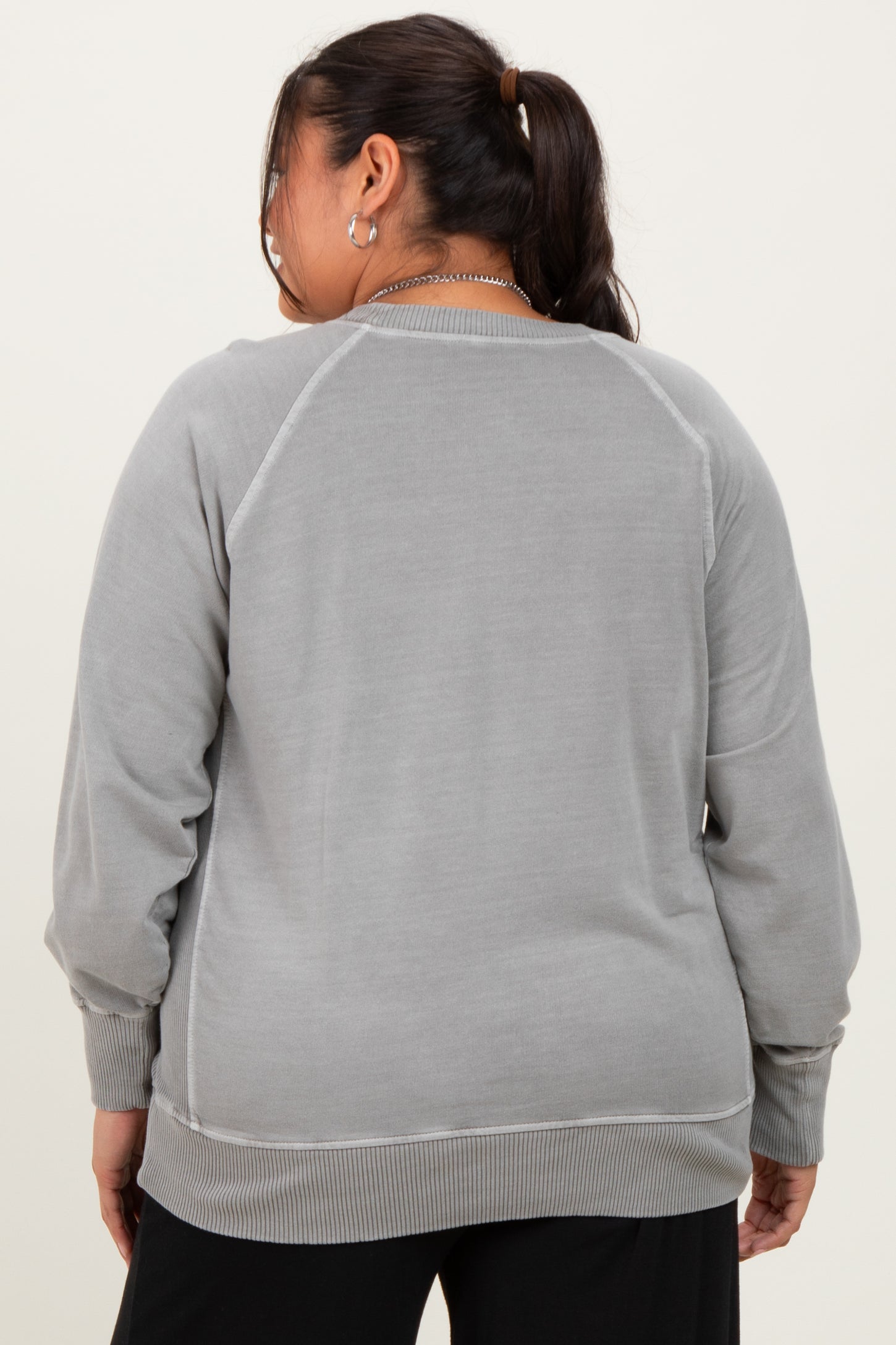 woman wearing a light grey plus size sweatshirt with ribbed cuffs and hem, viewed from the back