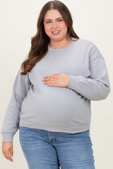 woman wearing a light gray maternity sweatshirt and holding her baby bump with a smiling expression